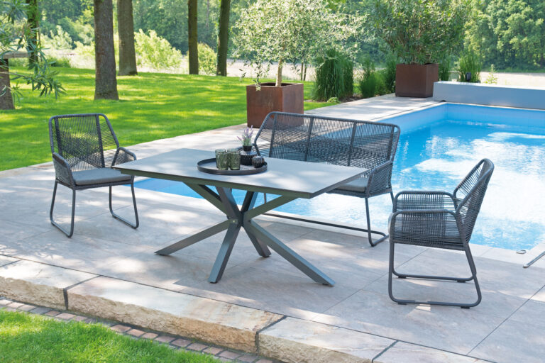 Gartenmöbel-Set am Pool mit grüner Umgebung, zwei Stühlen und einer Bank auf Steinfliesen.