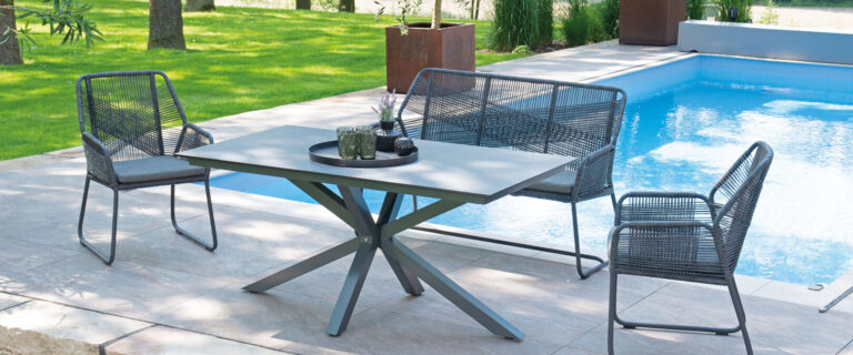 Gartenmöbel-Set am Pool mit grüner Umgebung, zwei Stühlen und einer Bank auf Steinfliesen.