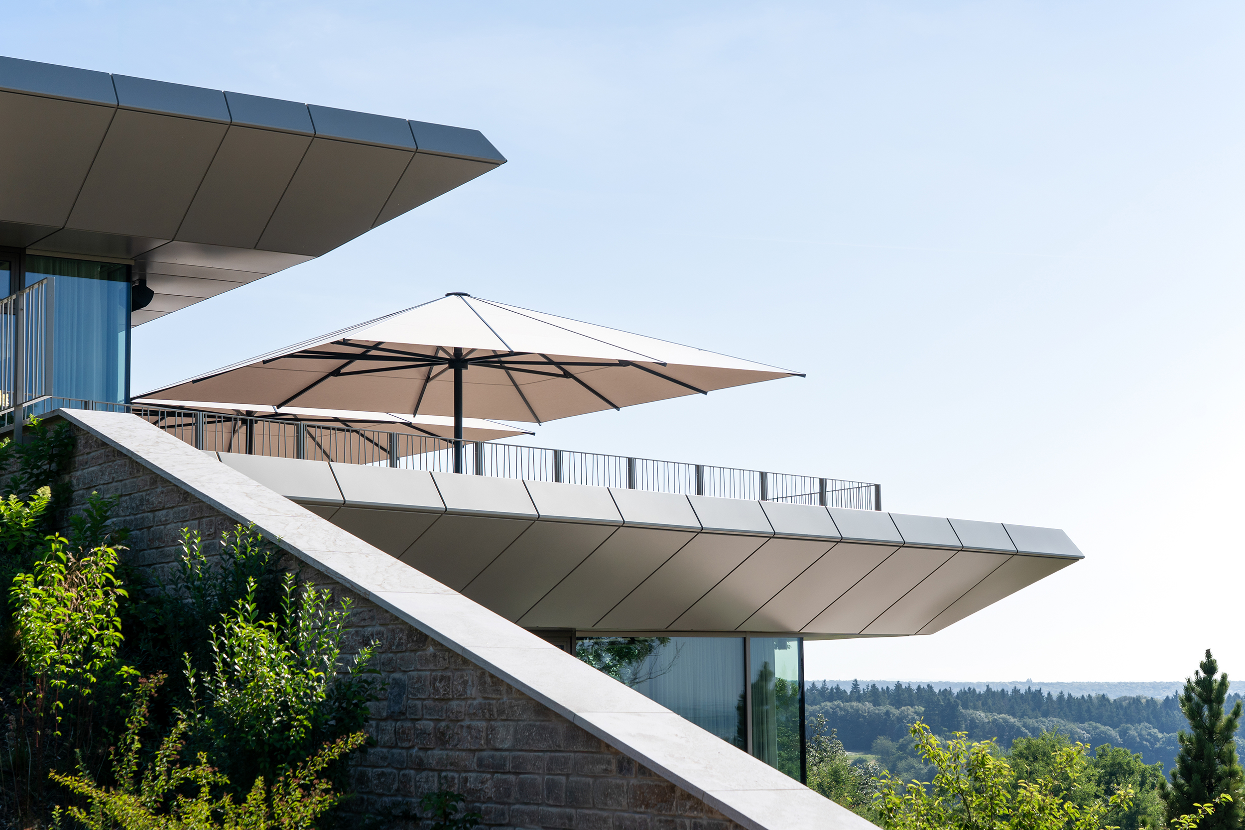 Eine moderne Terrasse mit großem, hellem Sonnenschirm und Ausblick ins Grüne