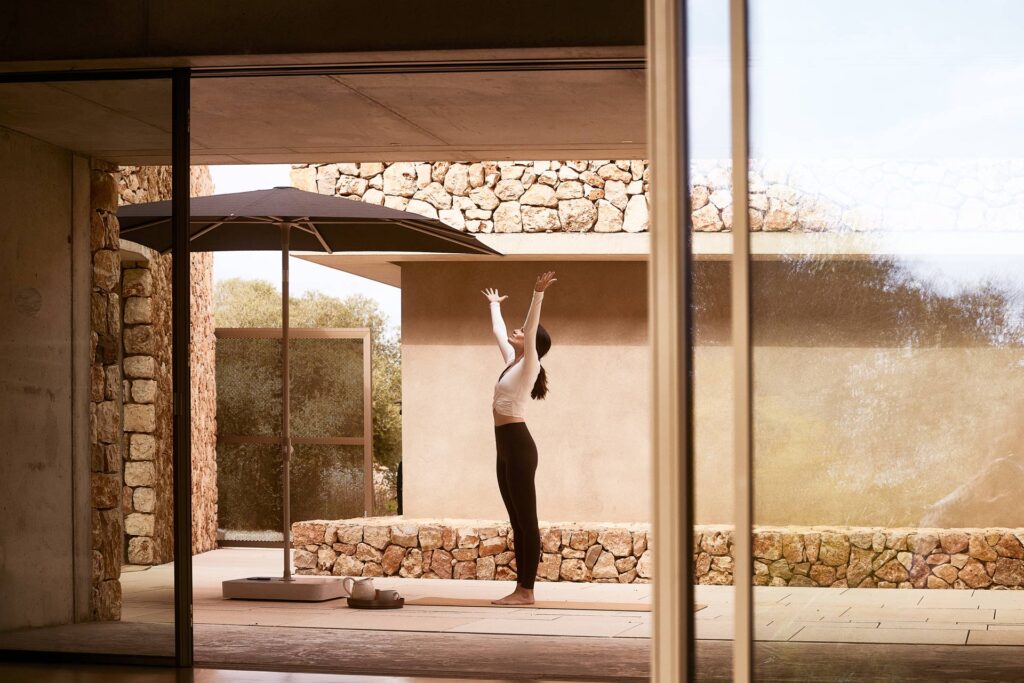 Eine Frau steht entspannt in Sportkleidung mit erhobenen Armen auf einer Terrasse