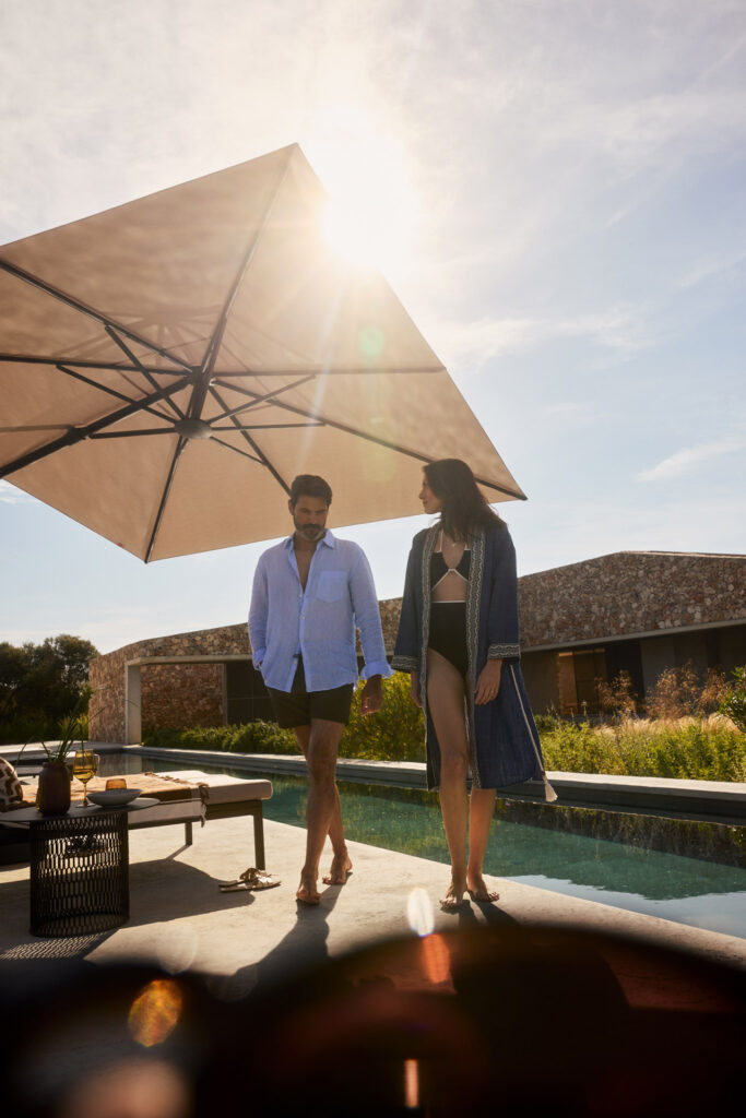 Ein Mann und eine Frau lächeln entspannt am Pool unter einem großen Sonnenschirm