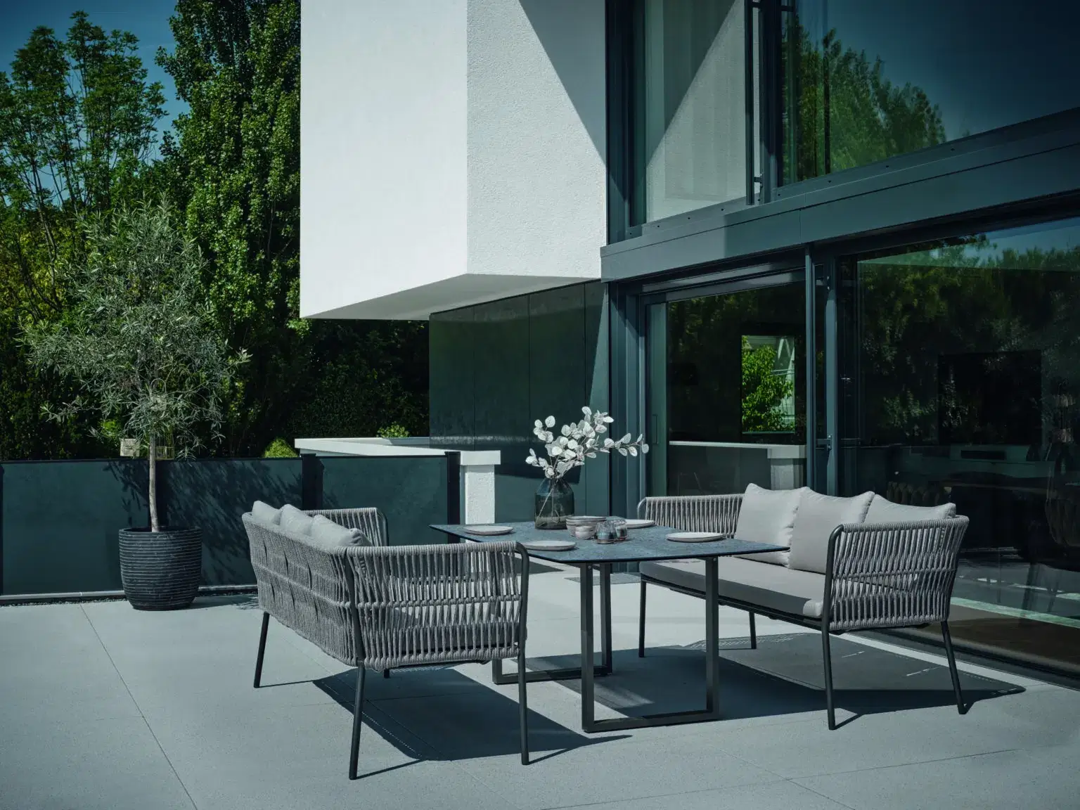Moderne Terrasse mit grauen Gartenmöbeln vor einem Haus mit großen Fenstern