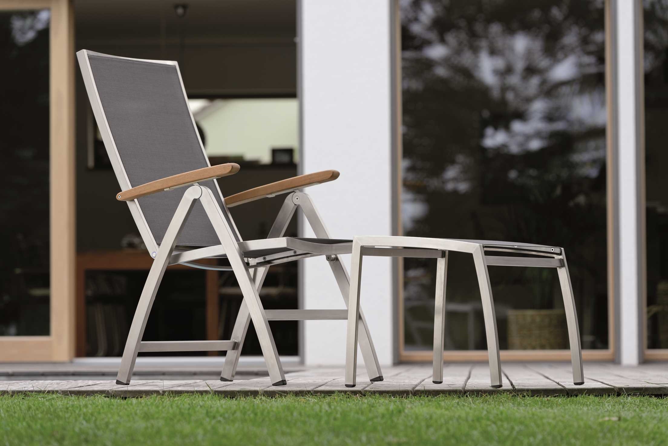 Ein moderner grauer Stuhl mit Holzarmlehnen steht vor einer Glastür auf einer Terrasse