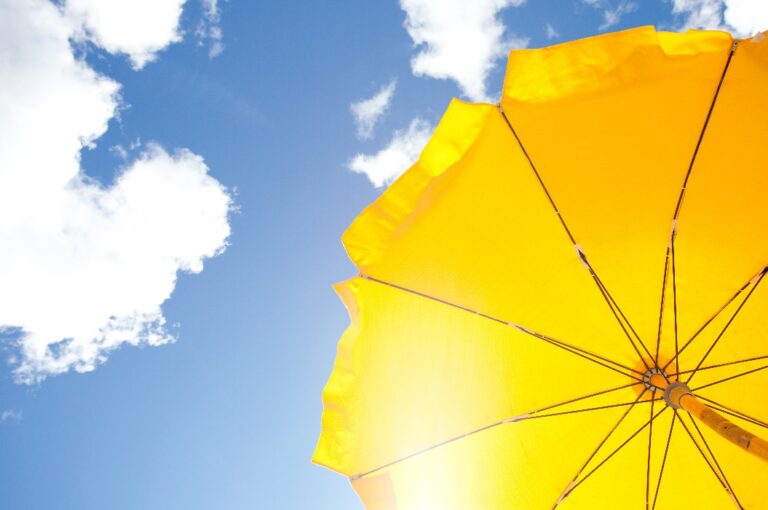 gelber Regenschirm vor blauem Himmel mit Wolken